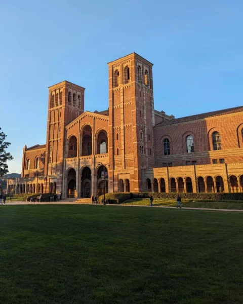 Royce Hall at UCLA in golden late-afternoon light, its two brick towers against a clear blue sky above the lawn.