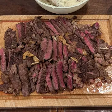 Sliced steak on a wooden board, with roasted broccoli, mashed potatoes and a green salad